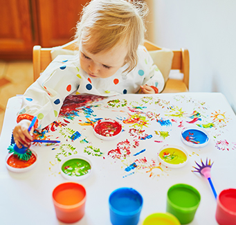 little girl sitting at a table painting