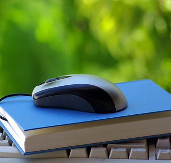 a computer keyboard with a book and a computer mouse stacked on it