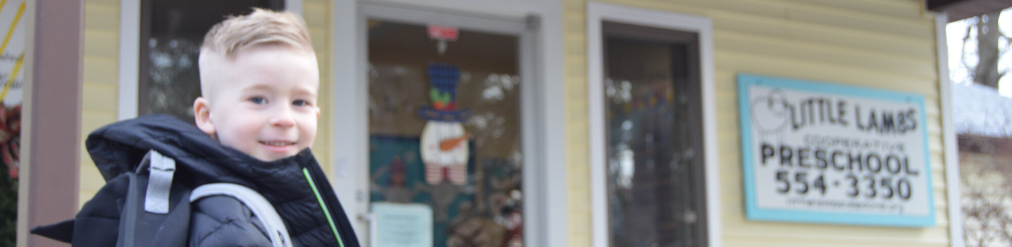 Boy standing in front of the Little Lambs Preschool building